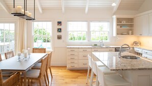 A modern kitchen with white cabinetry, a granite countertop, and a built-in sink. There are multiple windows providing natural light and a view of greenery outside. - Upscale Beach House Brant Point (Nantucket)
