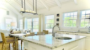A spacious kitchen with a large island, white cabinetry, and a dining area with wicker chairs. - Upscale Beach House Brant Point (Nantucket)