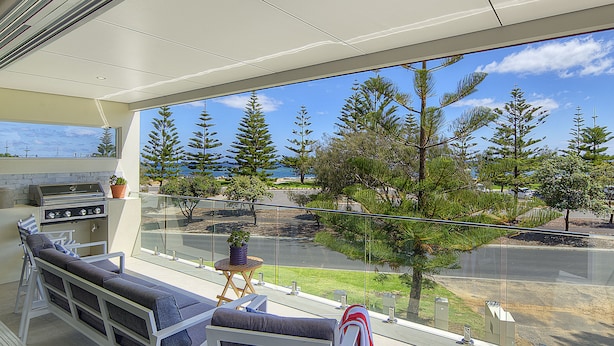 A balcony with a seating area, a grill, and a view of trees and a road. - Beachside 880  beachfront luxury Apartment with Sunset views from the balcony. (Busselton)