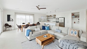 A modern living room with a sectional sofa, a wooden coffee table, and a dining area with a table and chairs. - Beachside 880  beachfront luxury Apartment with Sunset views from the balcony. (Busselton)