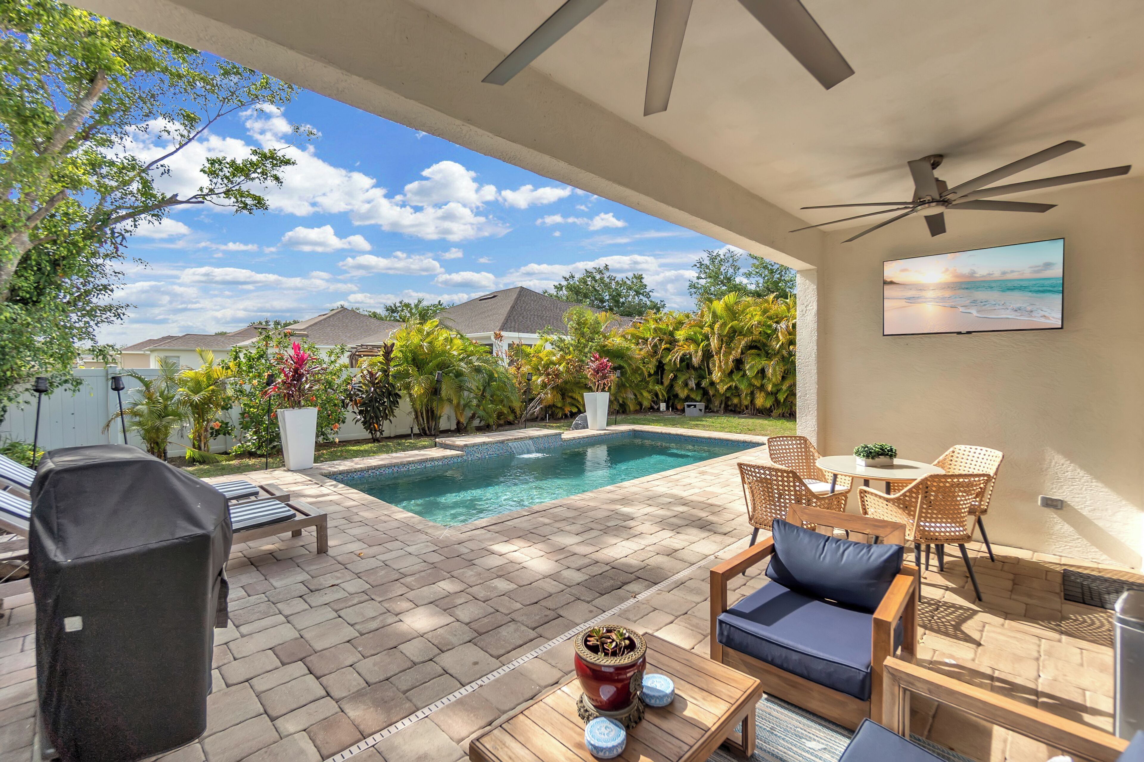 An outdoor patio with a pool, lounge chairs, a table with cushions, and a ceiling fan.