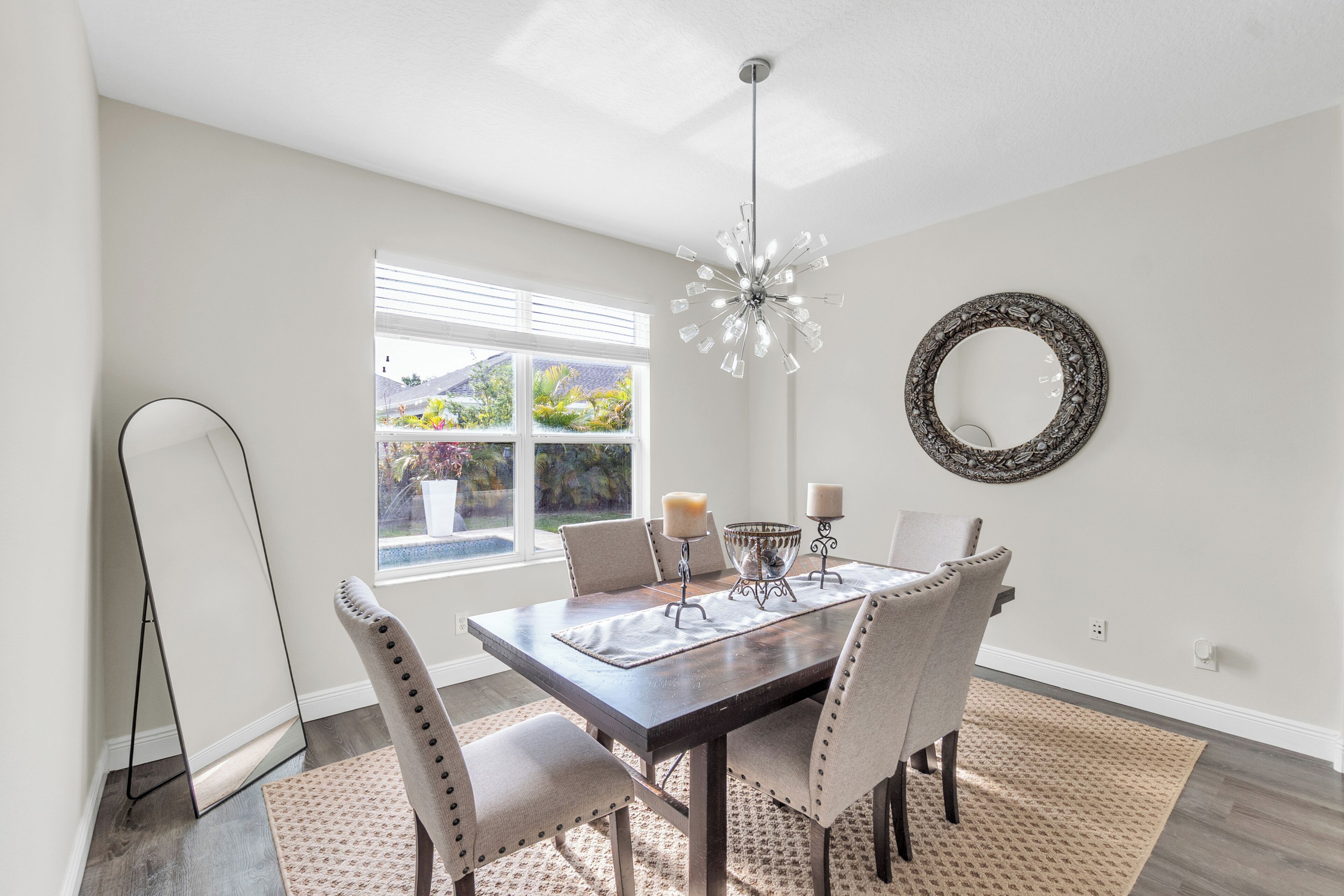 Un comedor con una mesa de madera oscura, sillas tapizadas en beige, una araña y un espejo decorativo en la pared.