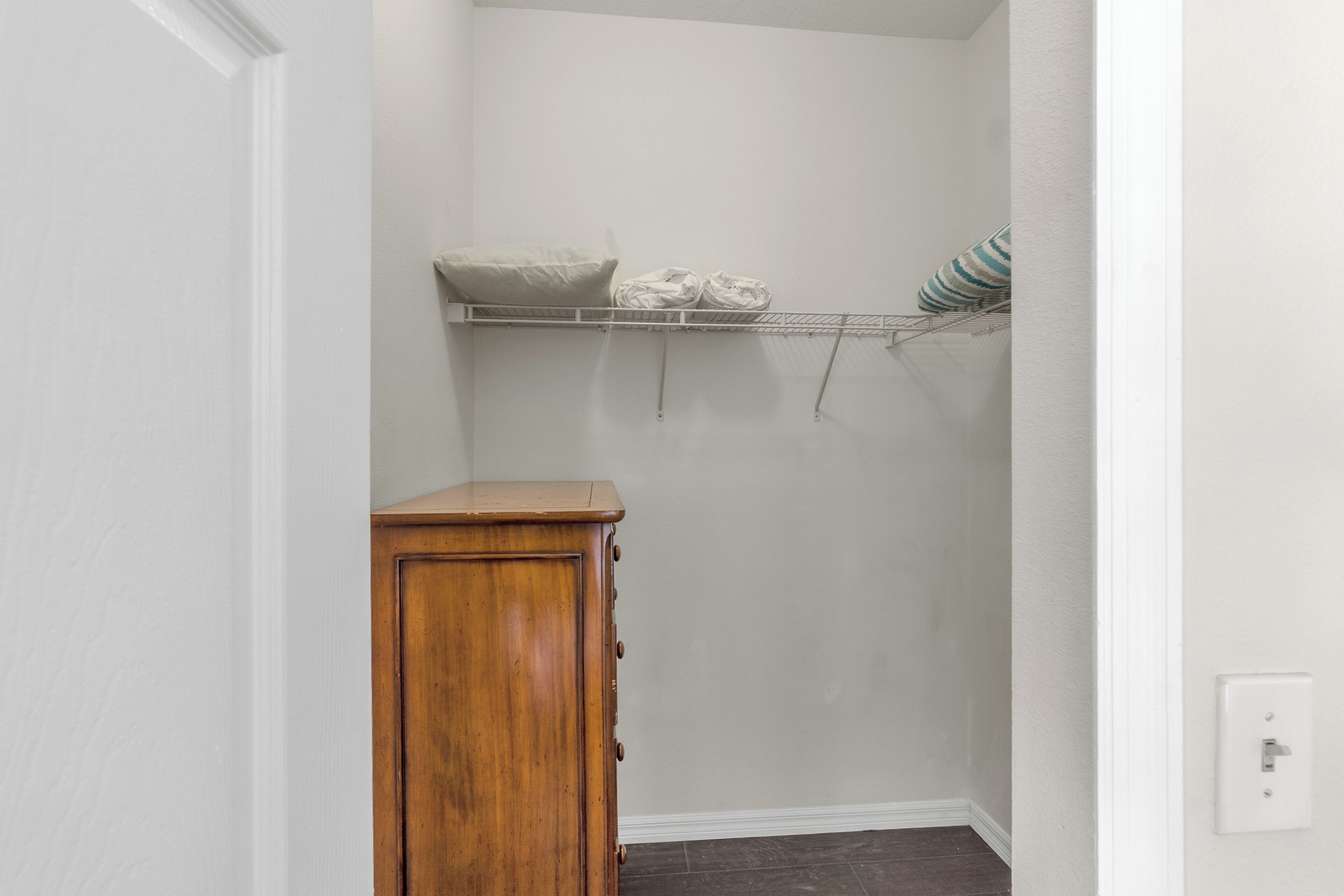 Un pasillo estrecho con un mueble de madera, una pared blanca y un estante con objetos doblados.