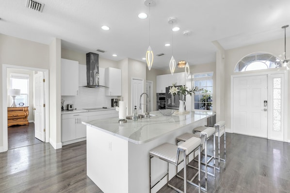 A modern kitchen with a large island, white cabinetry, stainless steel appliances, and pendant lighting.