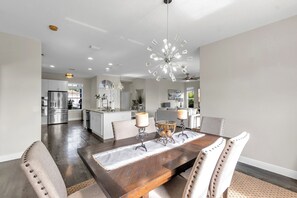 A spacious dining area with a wooden table, cushioned chairs, and a modern chandelier.