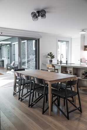 A modern kitchen with a wooden dining table and black chairs, a sink, and a potted plant.