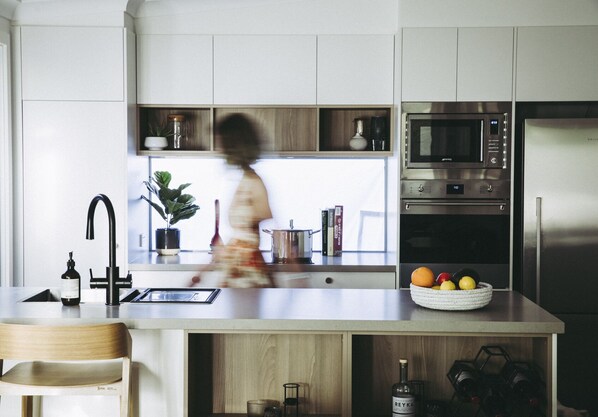 A modern kitchen with a stainless steel refrigerator, microwave, and oven. There is a wooden island with a sink and a potted plant.