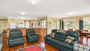A spacious living area with a green leather sofa, two matching armchairs, a wooden dining table, and a kitchen in the background.