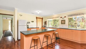 A kitchen with a central island, wooden bar stools, and a view of the outdoors through large windows.