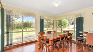 A dining room with a wooden table and chairs, large windows with curtains, and a view of the outdoors.