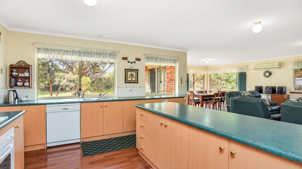 A kitchen with wooden cabinets, a dishwasher, and a large window with curtains. - Holiday Close to the Beach Park Swimming Centre (VICTOR HARBOR)