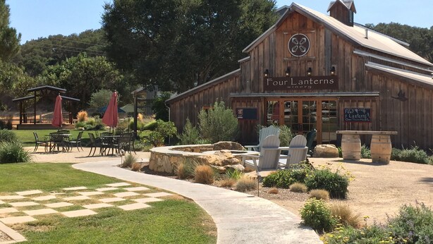 A rustic wooden building labeled "Four Lanterns Winery" with outdoor seating and a paved walkway. - The Farmhouse @ Four Lanterns Winery (Paso Robles)