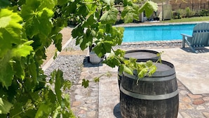A pool area with a stone patio, a wooden barrel, and lush green foliage. - The Farmhouse @ Four Lanterns Winery (Paso Robles)