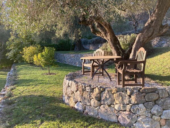 A stone bench with a table and chairs in a garden with a stone wall and trees. - Paradise in Provence- A Quiet Retreat (3BR) with Pool, Terrace, Barbecue, Garden (Tourrettes-Sur-Loup)