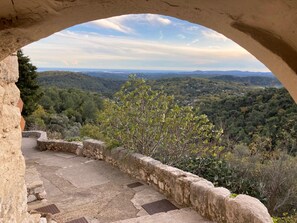 Un sentier de pierres mène à un belvédère offrant une vue panoramique sur une vallée boisée.