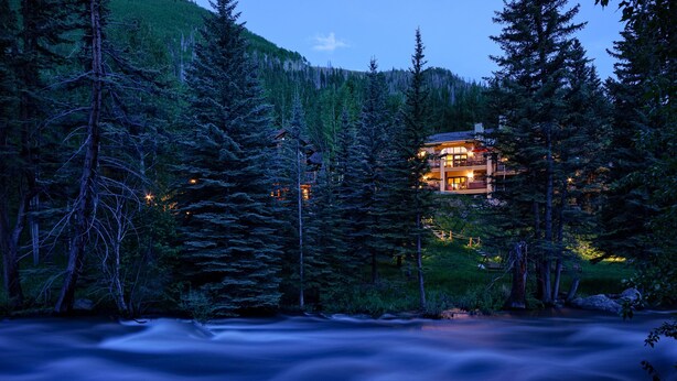 Eine Lodge, umgeben von dichtem Wald, mit einem Fluss im Vordergrund.