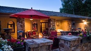 Eine Terrasse im Freien mit Steinmauern, einer Feuerstelle, roten Stühlen und einem roten Sonnenschirm.