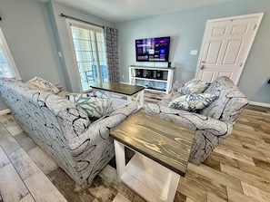 A living room with patterned sofas, a wooden coffee table, a TV, and a white entertainment unit.