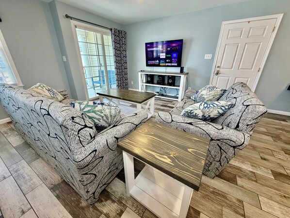 A living room with patterned sofas, a wooden coffee table, a TV, and a white entertainment unit. - Just Short Block Away from The Beach & Boadwalk (Wildwood)