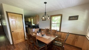 Un comedor con una mesa de madera, seis sillas, una araña y una cocina al fondo.