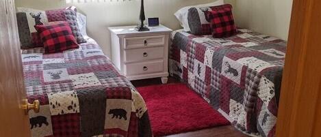 A bedroom with two beds, a nightstand, a lamp, and a window with blinds.