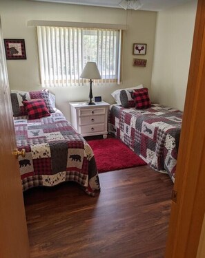 A bedroom with two beds, a nightstand, a lamp, and a window with blinds.