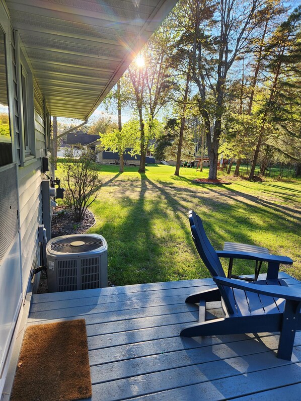 A covered porch with a rocking chair, a small air conditioning unit, and a grassy yard with trees.