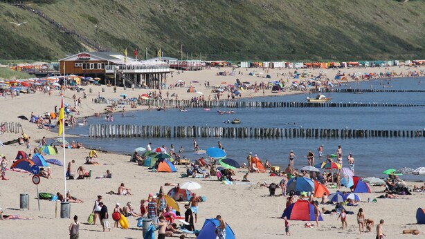 Ein Strand mit Zelten, Sonnenschirmen und Menschen.