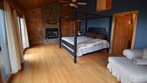 A cozy bedroom with a four-poster bed, a stone fireplace, and a ceiling fan.