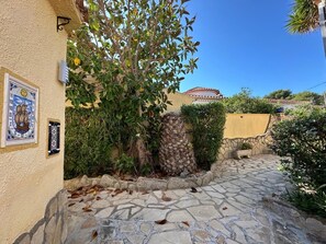 A stone-paved courtyard with a tree, a wall with a decorative plate, and a building with a tiled roof.