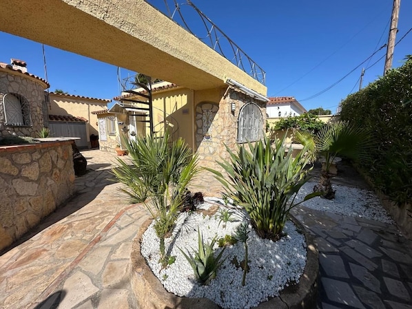 Une cour bordée de murs en pierre, agrémentée de jardinières en gravier blanc, et surplombée d’un ciel d’un bleu limpide.