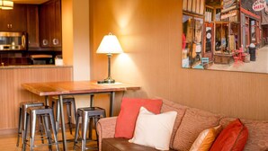 Un salon chaleureux avec un canapé en cuir marron, une table basse en bois et un tableau représentant une scène de rue accroché au mur.