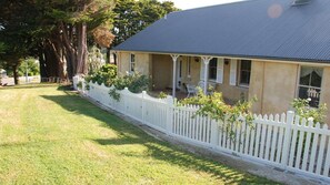 A house with a white picket fence, a covered porch, and a well-maintained lawn. - Hillside Cottage - historic 1843 attached cottage in an AWARD WINNING village (Berrima)