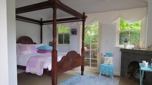 Ein Bett mit Baldachin, dessen Gestell aus Holz besteht, ein kleiner Tisch mit blauer Tischdecke sowie ein Kamin.