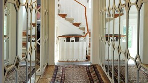 A hallway with patterned carpet, white decorative railings, and a staircase in the background.