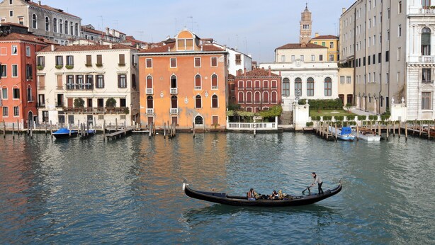 A canal with a gondola, historic buildings, and a clear sky.