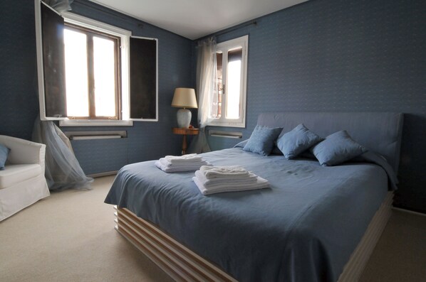 A bedroom with a bed, two windows, a bedside table with a lamp, and a chair. - Breathtaking view on the Grand Canal and Guggenheim's garden (Venezia)