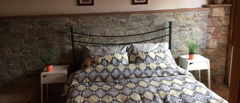 Un lit recouvert d’une couvre-lit à motifs, deux tableaux encadrés accrochés au mur et un mur en pierre derrière le lit.