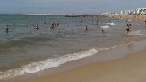 A beach with people swimming and walking along the shore.