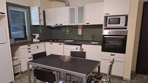 A compact kitchen with white cabinets, a microwave, an oven, and a sink. There is a dining table with chairs and a bowl on it.