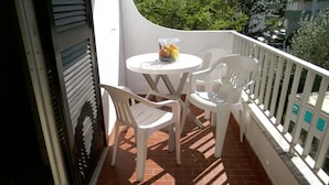 A balcony with a white table and two white chairs, a small round table with a fruit container, and a white railing with a sign.