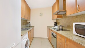 Cocina compacta con armarios de madera, lavadora, microondas y estufa.