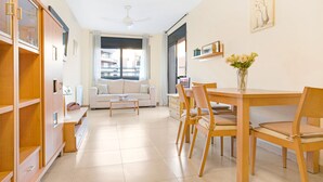 Una sala moderna con un sofá, una mesa de comedor, sillas y una mesa de centro. Hay una estantería, un ventanal con vistas y un ventilador de techo.