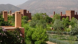Un edificio tradicional de adobe con múltiples torres, rodeado de exuberante vegetación y montañas al fondo.