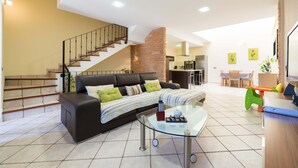 Ein modernes Wohnzimmer mit einer schwarzen Ledersofa, einem Glastisch und einer Treppe, die zu einer oberen Etage führt.