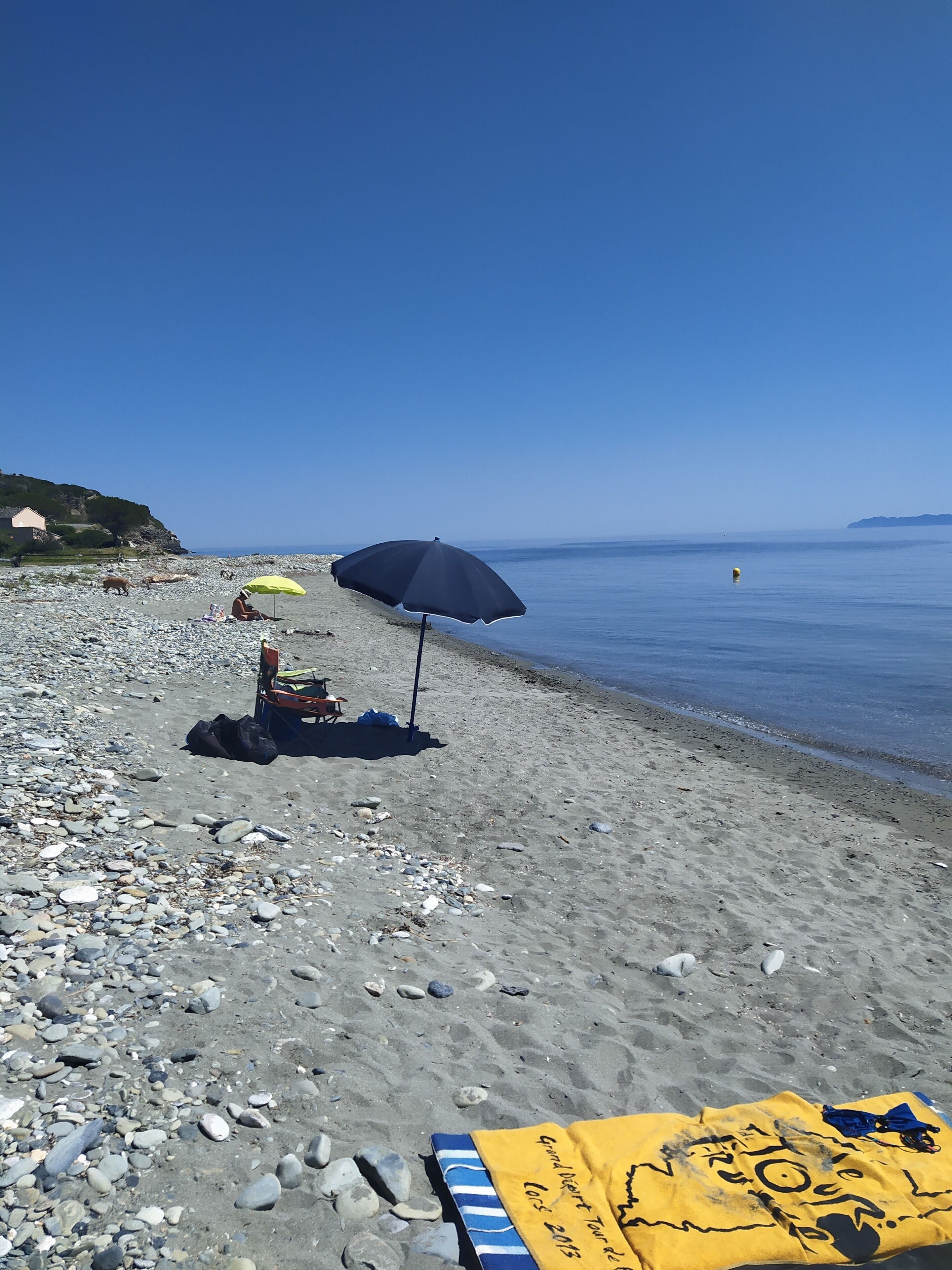 A pebbled beach with a yellow towel and a black umbrella.