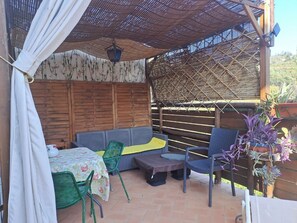 An outdoor patio with a wooden fence, a covered seating area with cushions, and a table with chairs. - Cozy rustico on Versilia green hills, sea view, air cond, WIFI, 12 km sea, Lucca (Montigiano, Massarosa)