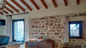 Una stanza rustica con parete in pietra, mobili in legno, un laptop su un tavolo e una ciotola di frutta.