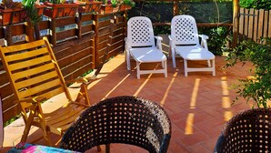 Un patio con due sedie bianche, una sedia in vimini e un tavolo con tovaglia a fiori.