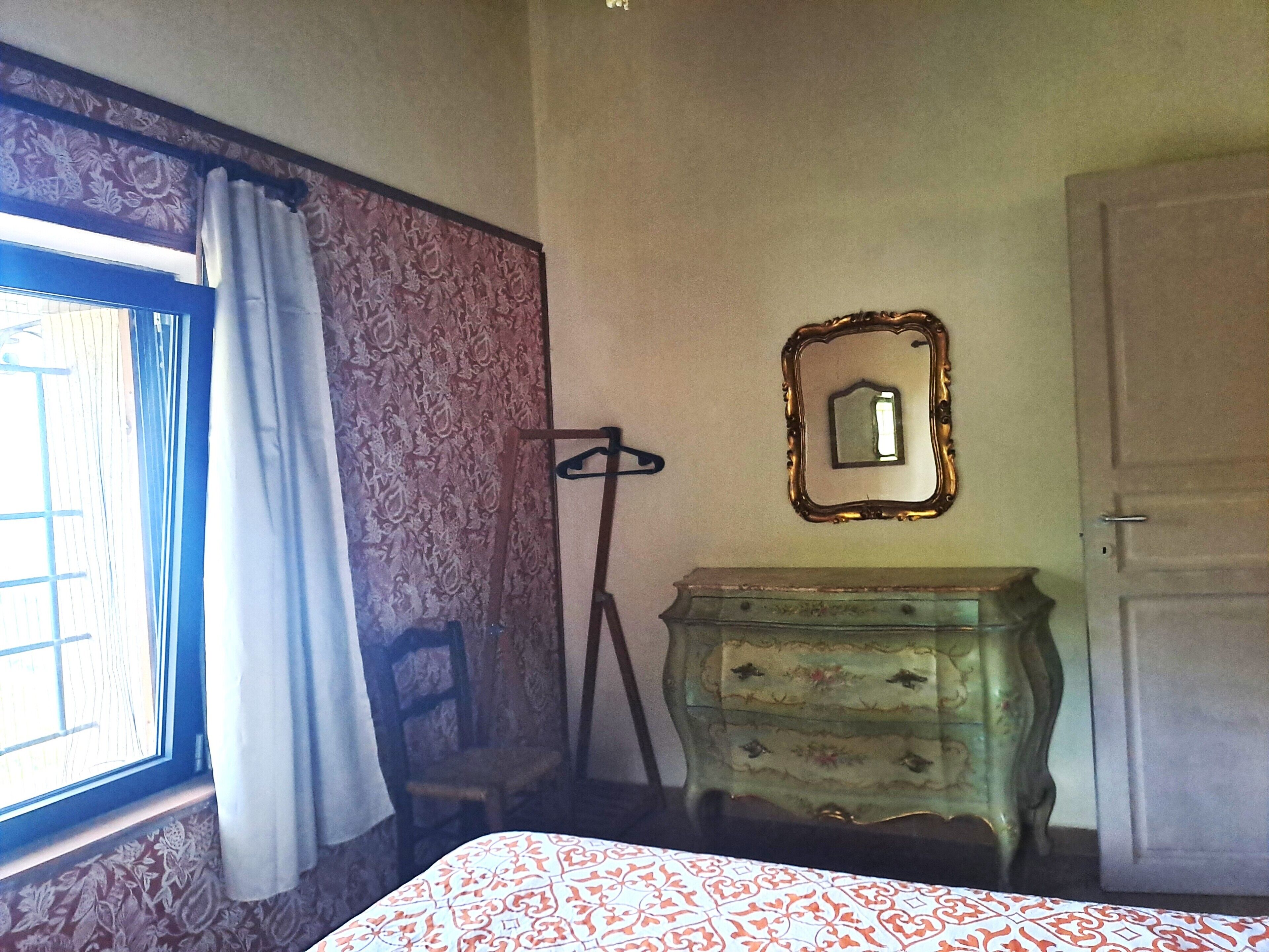 A room with a bed, a dresser, a mirror, a window with curtains, and a door.